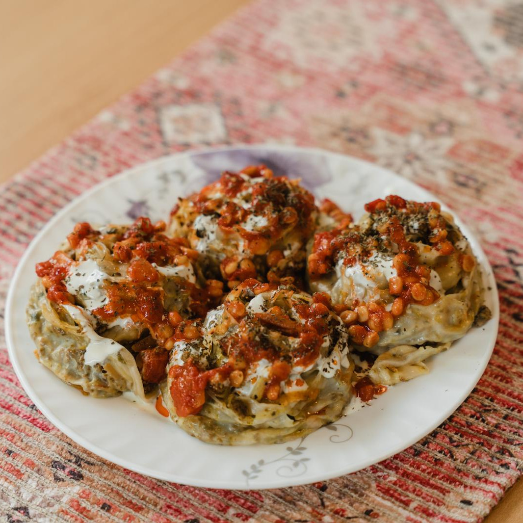Four Afghan mantu dumplings with tomato sauce, yogurt and lentils on a flowered plate, on a carpet runner