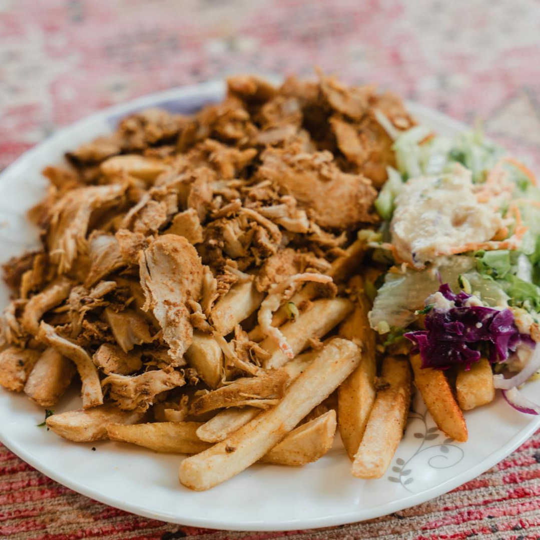 A plate piled with spiced shredded chicken over chips, with salad and garlic sauce, on a carpet runner