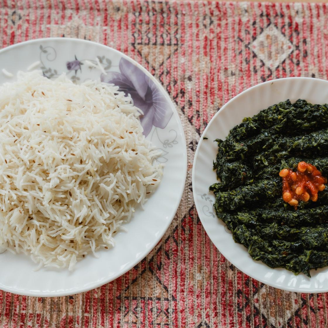 A mound of cumin basmati rice beside a plate of dark slow-cooked spinach topped with chickpeas in chilli, on a red carpet runner
